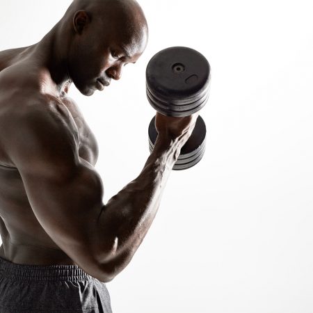 Shot of healthy muscular young man doing weight exercise with dumbbells against grey background. Bodybuilder doing heavy weight workout for biceps.